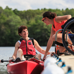 Female kayaker with disability near dock containing wheelchair and instructor.